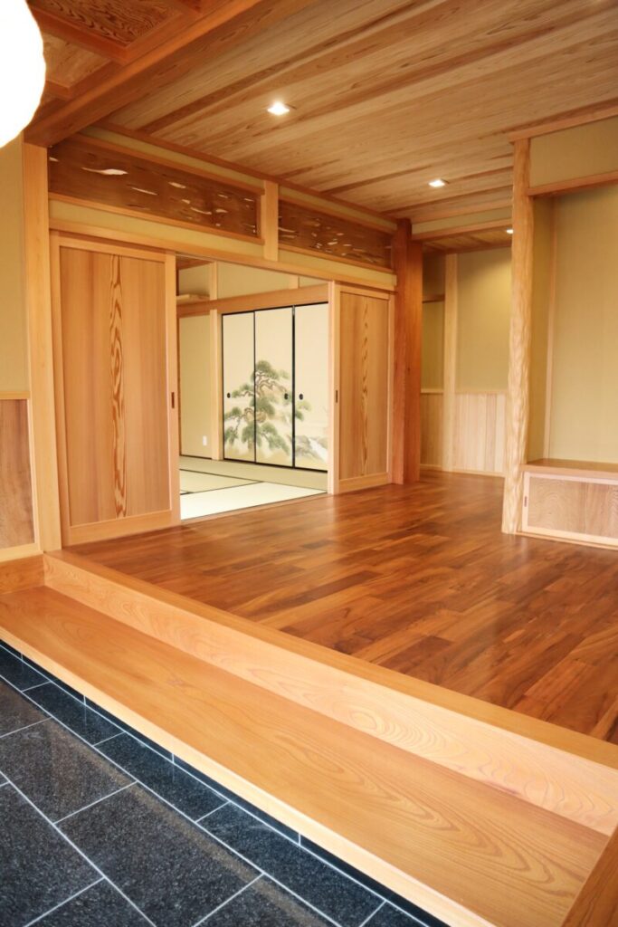 玄関の土間から木の床へ続く和の室内。障子と松の絵柄の建具、木の天井が落ち着いた雰囲気をつくる。