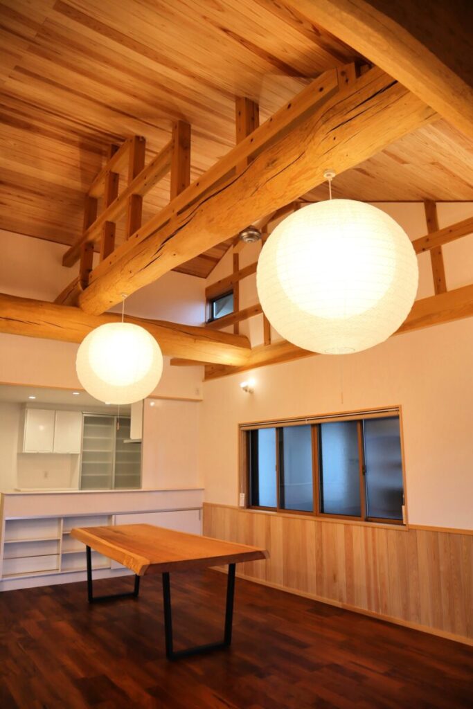 木の梁と板張り天井が広がる室内空間。丸い照明が柔らかく灯り、無垢材のテーブルと木の質感を生かした内装が落ち着いた雰囲気をつくる。