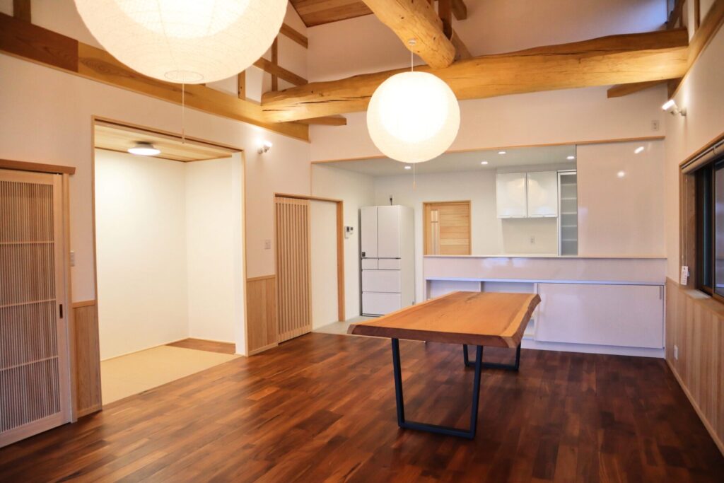 木の梁と板張り天井が広がる室内空間。丸い照明が柔らかく灯り、無垢材のテーブルと木の質感を生かした内装が落ち着いた雰囲気をつくる。