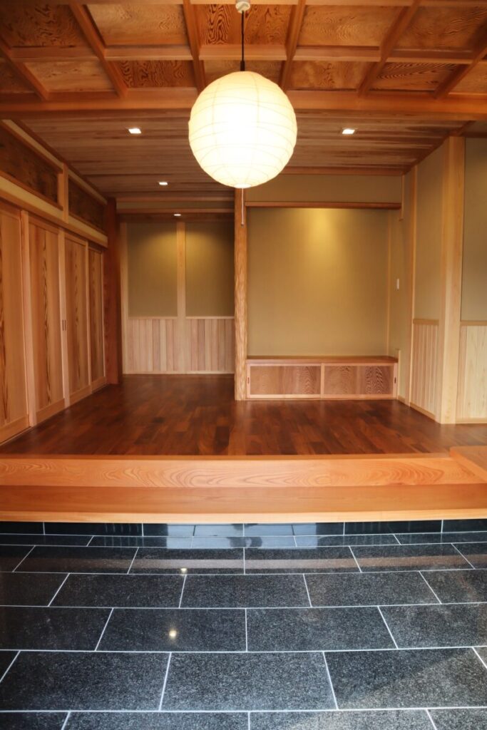 土間から木の床へ続く和の玄関空間。丸い照明と木の天井、造作収納が落ち着いた雰囲気をつくる。